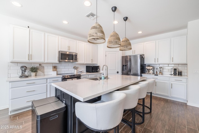 kitchen featuring a center island with sink, appliances with stainless steel finishes, sink, white cabinetry, and decorative light fixtures