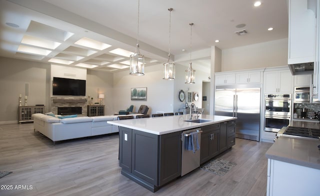 kitchen featuring pendant lighting, appliances with stainless steel finishes, white cabinetry, an island with sink, and beam ceiling