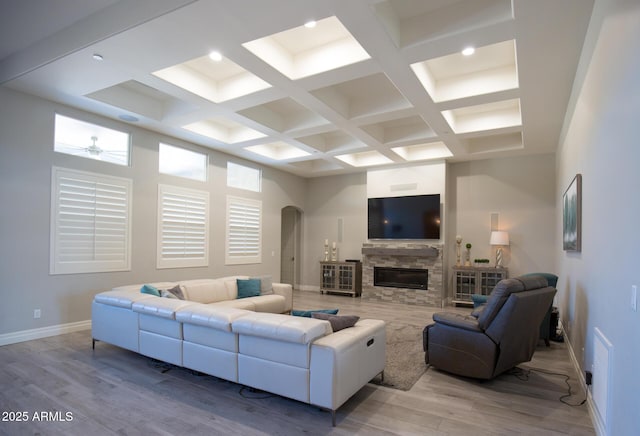 living room featuring beam ceiling, a fireplace, coffered ceiling, and light hardwood / wood-style floors