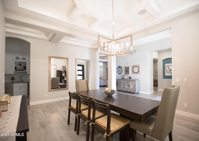 dining space featuring beam ceiling, light hardwood / wood-style flooring, coffered ceiling, and a notable chandelier