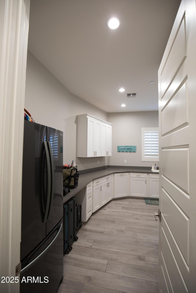 kitchen featuring black refrigerator, white cabinetry, and light hardwood / wood-style floors