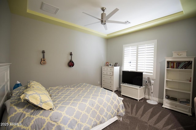 bedroom with ceiling fan, dark carpet, and a raised ceiling