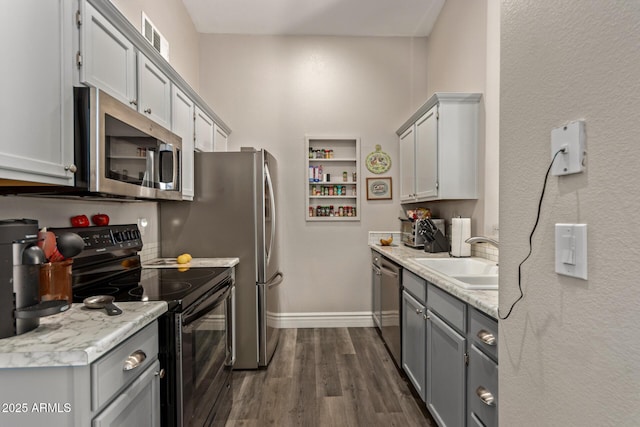 kitchen with sink, dark wood-type flooring, gray cabinetry, stainless steel appliances, and light stone countertops