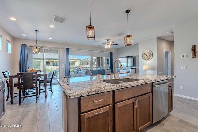 kitchen featuring light wood-type flooring, light stone counters, stainless steel dishwasher, a kitchen island with sink, and sink