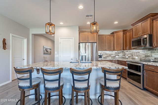 kitchen featuring light hardwood / wood-style floors, stainless steel appliances, hanging light fixtures, and an island with sink