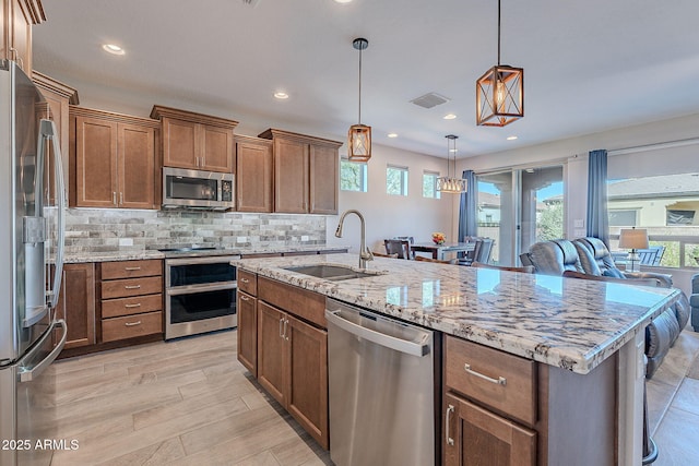 kitchen with appliances with stainless steel finishes, a center island with sink, hanging light fixtures, and a healthy amount of sunlight