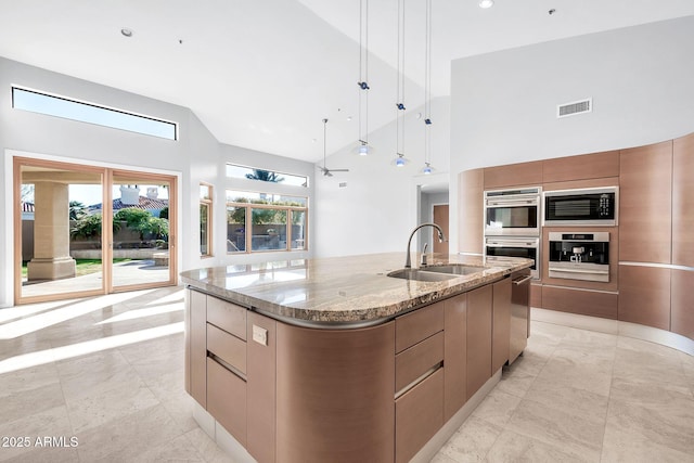 kitchen featuring sink, light stone counters, appliances with stainless steel finishes, pendant lighting, and a large island