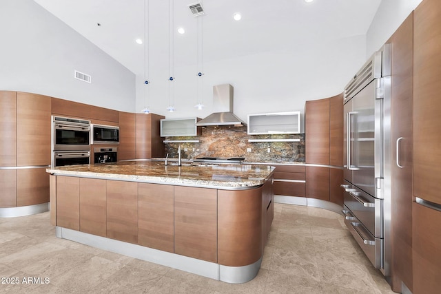 kitchen featuring pendant lighting, a large island, appliances with stainless steel finishes, decorative backsplash, and wall chimney exhaust hood