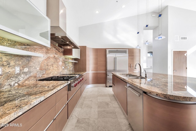 kitchen featuring wall chimney range hood, sink, hanging light fixtures, stainless steel appliances, and stone countertops