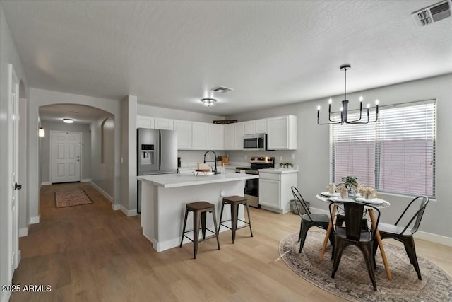 kitchen with sink, stainless steel appliances, white cabinets, a center island with sink, and decorative light fixtures