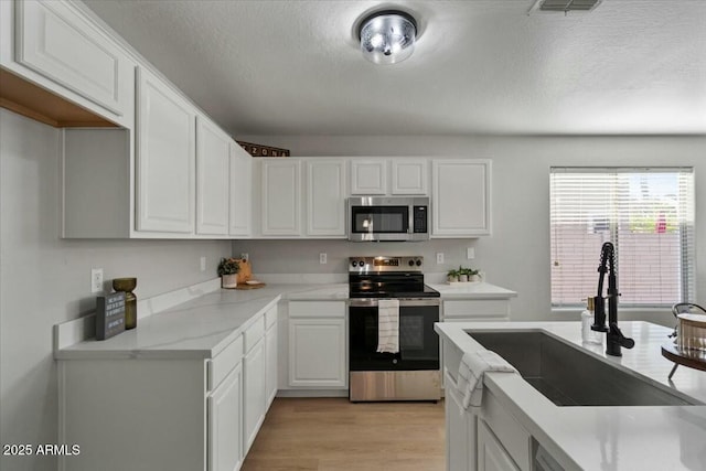 kitchen featuring sink, a textured ceiling, appliances with stainless steel finishes, light hardwood / wood-style floors, and white cabinets