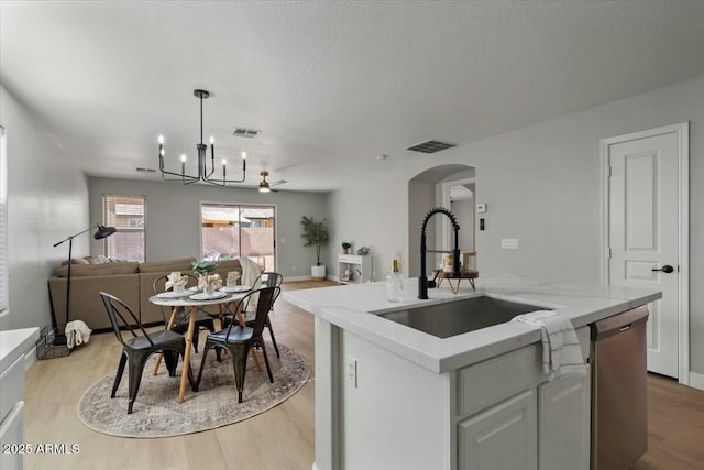 kitchen with dishwasher, an island with sink, sink, hanging light fixtures, and light hardwood / wood-style flooring