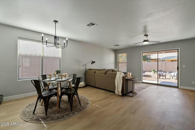 dining area with ceiling fan with notable chandelier, a textured ceiling, and light wood-type flooring