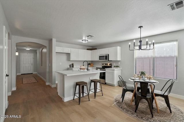 kitchen with stainless steel appliances, white cabinetry, sink, and an island with sink