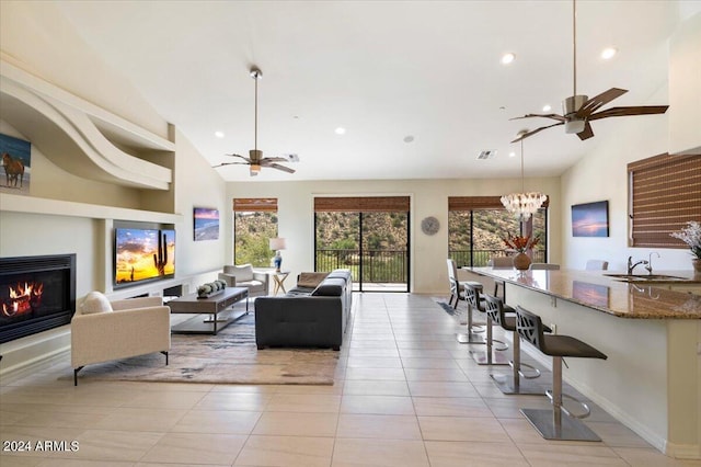 living room featuring light tile patterned floors, high vaulted ceiling, sink, and ceiling fan with notable chandelier