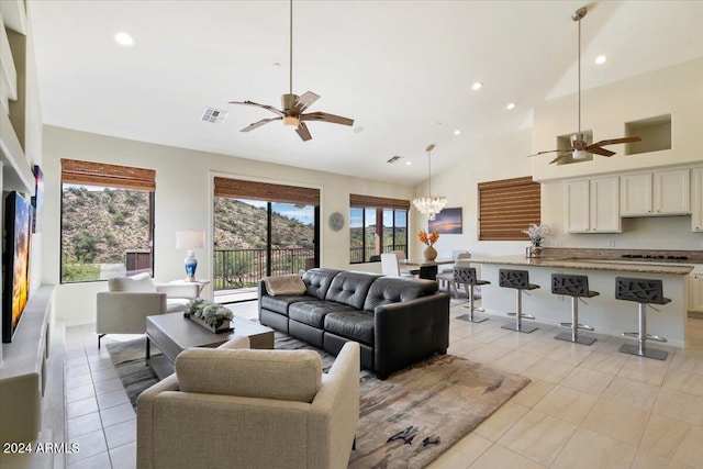 tiled living room featuring high vaulted ceiling and ceiling fan with notable chandelier