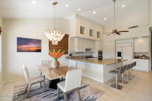 kitchen featuring built in appliances, kitchen peninsula, dark stone countertops, pendant lighting, and high vaulted ceiling