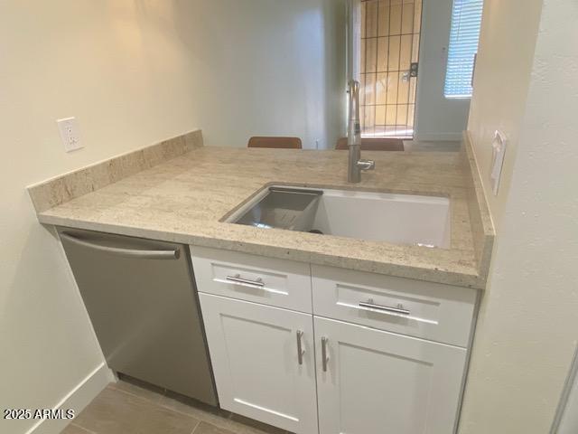 kitchen featuring stainless steel dishwasher, white cabinets, a sink, light stone countertops, and tile patterned floors