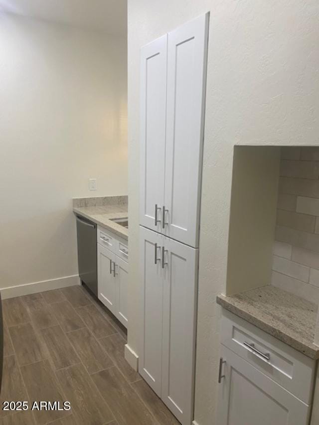 kitchen featuring stainless steel dishwasher, wood tiled floor, white cabinetry, light stone countertops, and baseboards