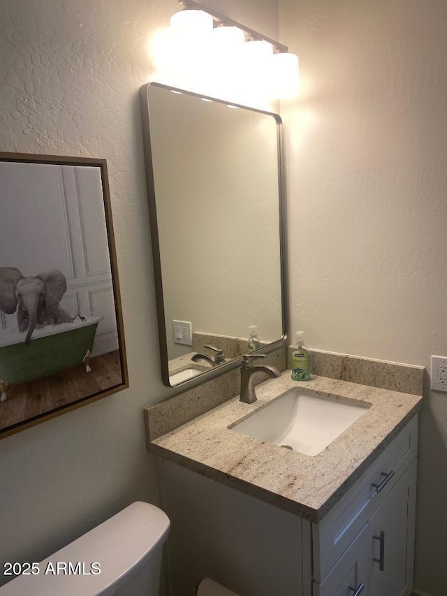 half bathroom with toilet, a textured wall, and vanity