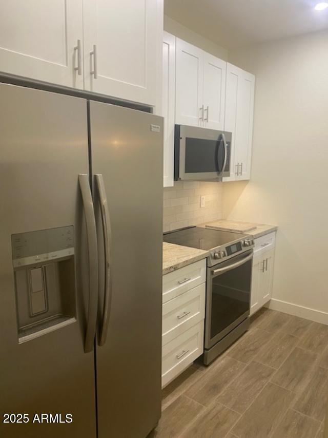 kitchen with appliances with stainless steel finishes, wood finished floors, light stone countertops, white cabinetry, and backsplash