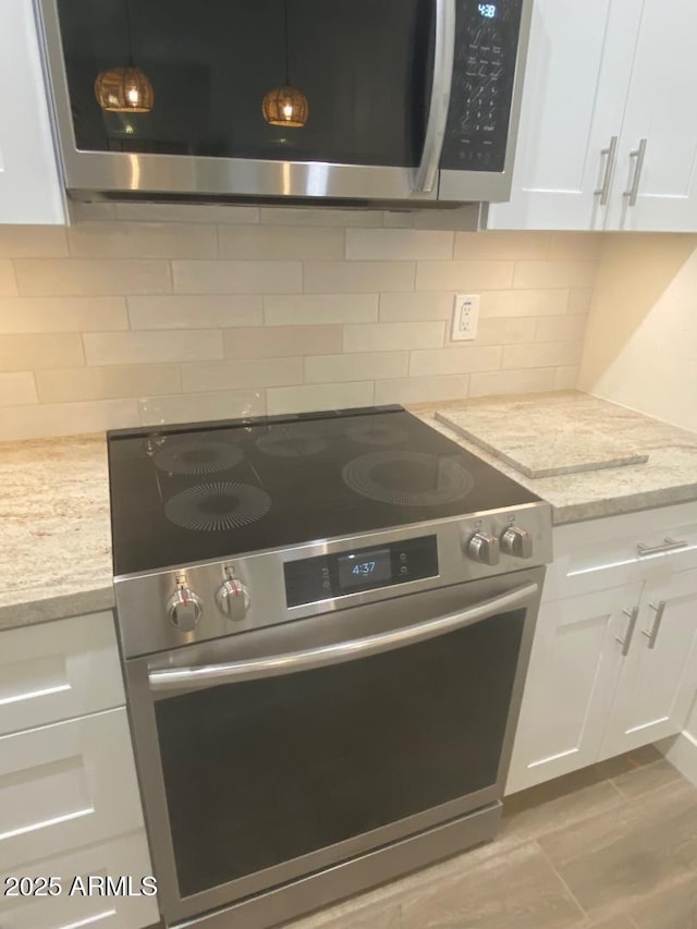 kitchen featuring stainless steel appliances, backsplash, white cabinetry, and light stone countertops