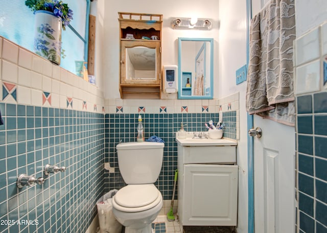 bathroom with wainscoting, toilet, tile patterned flooring, vanity, and tile walls