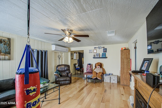 sitting room with a textured ceiling, a wall mounted air conditioner, wood finished floors, and a ceiling fan