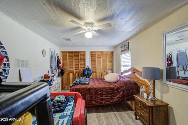 bedroom with two closets, visible vents, a ceiling fan, a textured ceiling, and wood finished floors