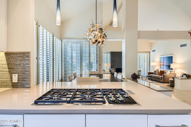 kitchen with a high ceiling, stainless steel gas cooktop, pendant lighting, and white cabinets