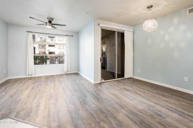 empty room with ceiling fan with notable chandelier, visible vents, baseboards, and wood finished floors