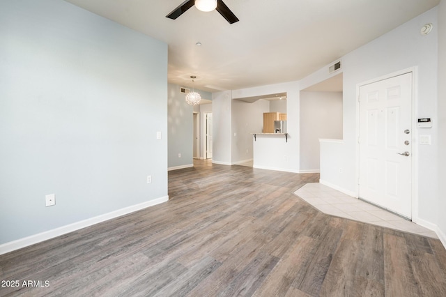 unfurnished living room with baseboards, visible vents, wood finished floors, and ceiling fan with notable chandelier