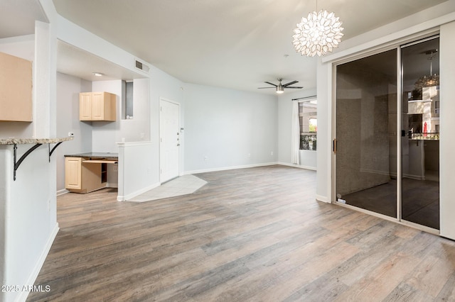 unfurnished dining area featuring light wood-style floors, baseboards, visible vents, and ceiling fan with notable chandelier