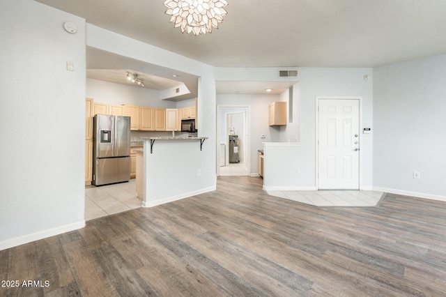 kitchen with visible vents, light wood-style flooring, a breakfast bar area, light brown cabinetry, and stainless steel refrigerator with ice dispenser