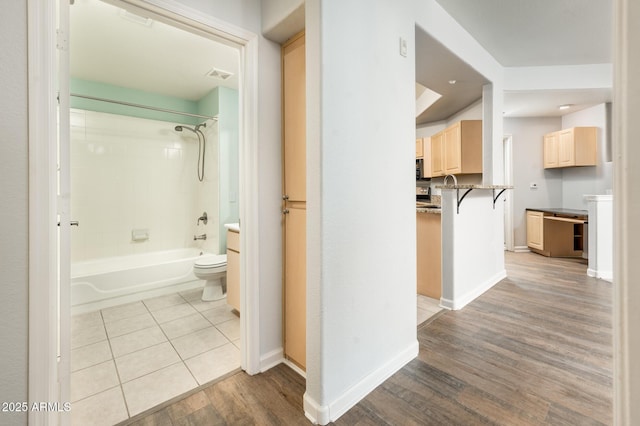 bathroom with bathing tub / shower combination, toilet, vanity, wood finished floors, and baseboards