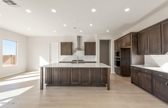 kitchen with stainless steel appliances, wall chimney range hood, tasteful backsplash, and a kitchen island with sink