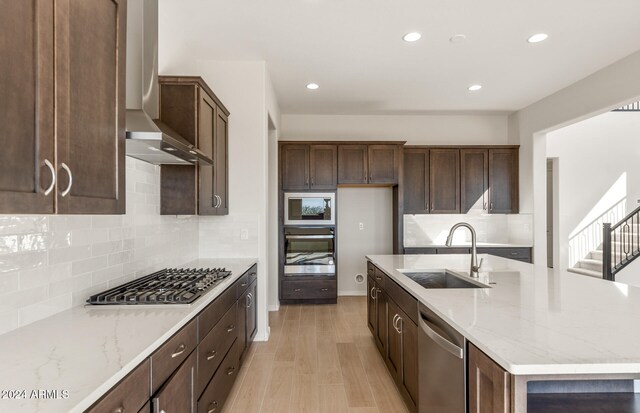 kitchen with light stone counters, wall chimney exhaust hood, sink, light hardwood / wood-style floors, and appliances with stainless steel finishes