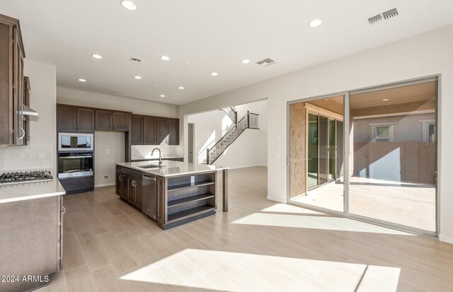 kitchen featuring sink, light hardwood / wood-style floors, appliances with stainless steel finishes, dark brown cabinets, and a center island with sink