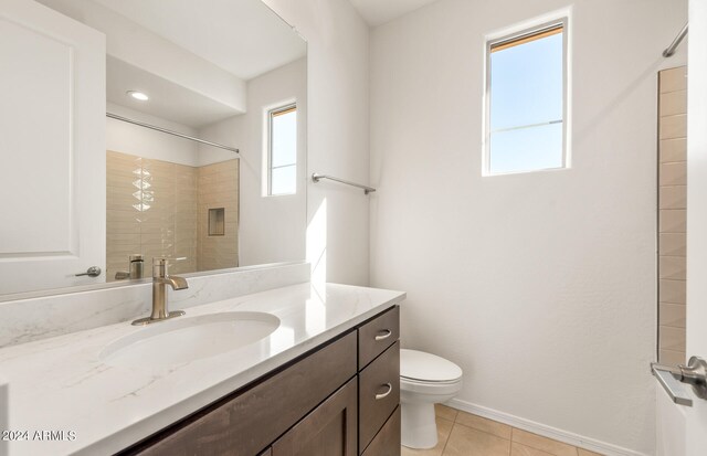 bathroom with tile patterned flooring, tiled shower, vanity, and toilet