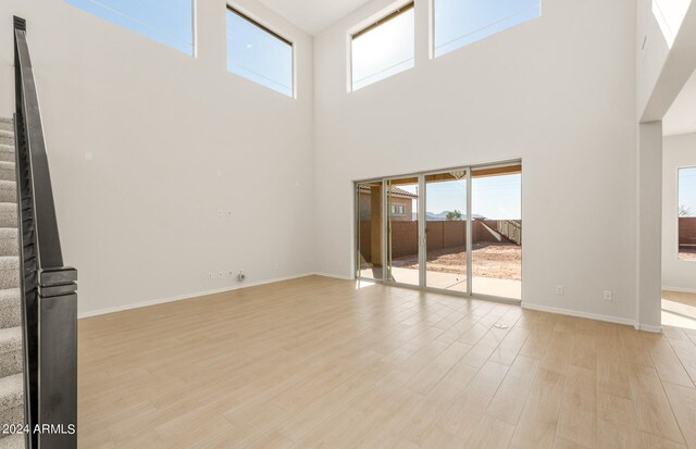 unfurnished living room featuring light wood-type flooring and a towering ceiling