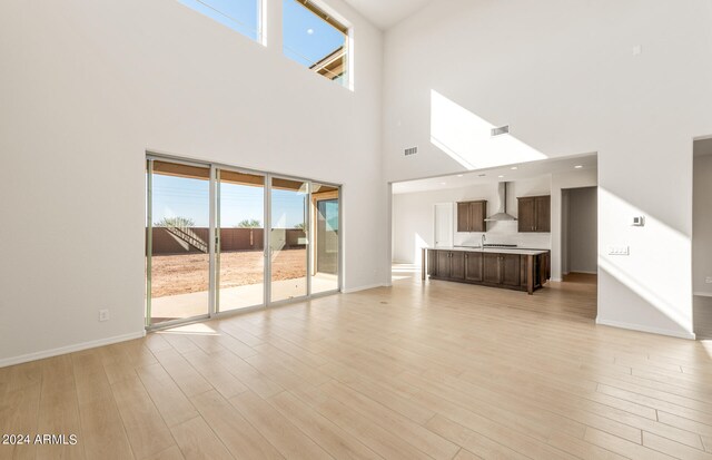 unfurnished living room with a high ceiling, light wood-type flooring, and a skylight