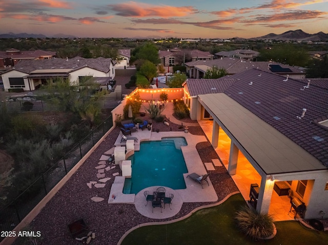 pool at dusk featuring a mountain view, a fenced backyard, a community pool, and a patio area