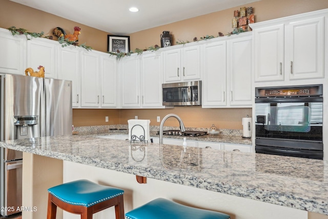 kitchen featuring a kitchen breakfast bar, white cabinets, light stone countertops, and appliances with stainless steel finishes