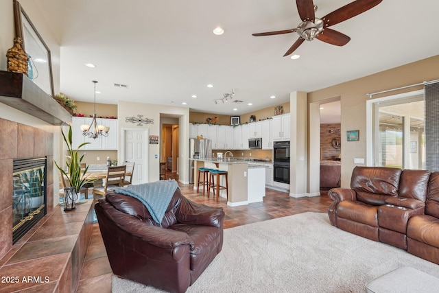 living room featuring visible vents, dark tile patterned floors, recessed lighting, a tiled fireplace, and ceiling fan with notable chandelier