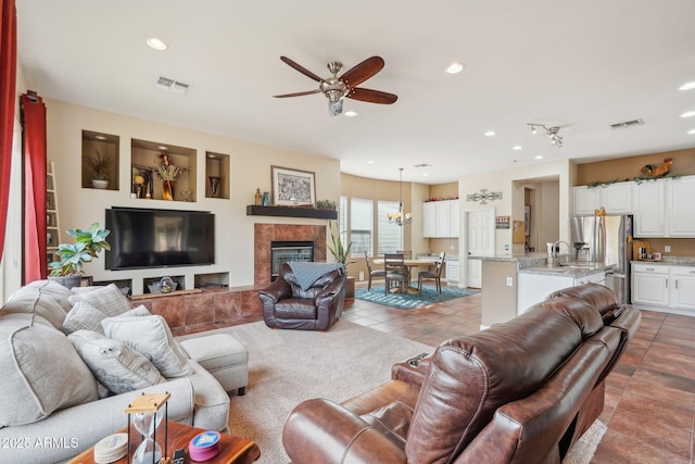 living area with visible vents, tile patterned flooring, ceiling fan with notable chandelier, and a tile fireplace