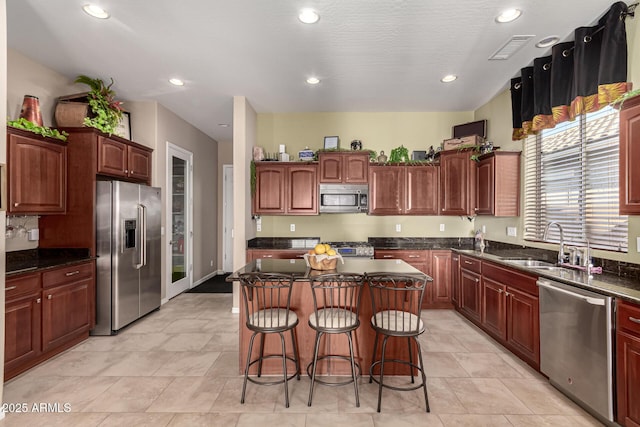 kitchen with sink, a breakfast bar area, dark stone counters, a kitchen island, and stainless steel appliances