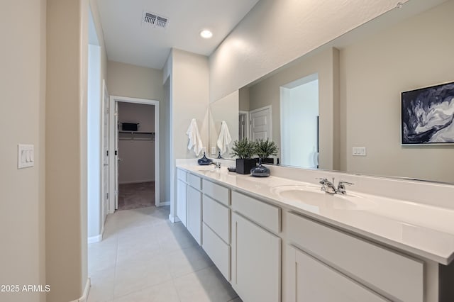 bathroom featuring visible vents, double vanity, a sink, tile patterned flooring, and a walk in closet