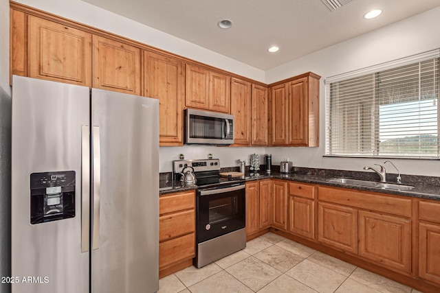 kitchen featuring dark stone countertops, stainless steel appliances, sink, and light tile patterned floors