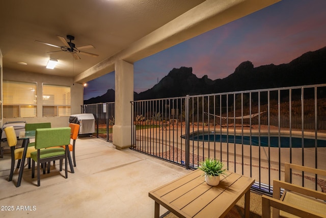 patio terrace at dusk featuring ceiling fan, grilling area, and a fenced in pool