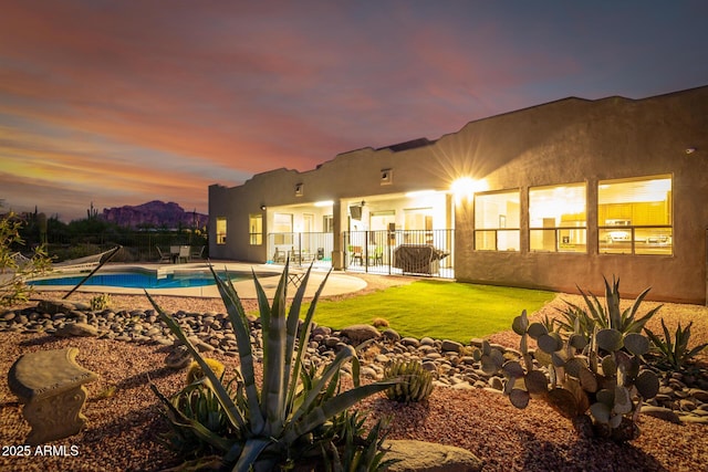 pool at dusk featuring a patio and a lawn